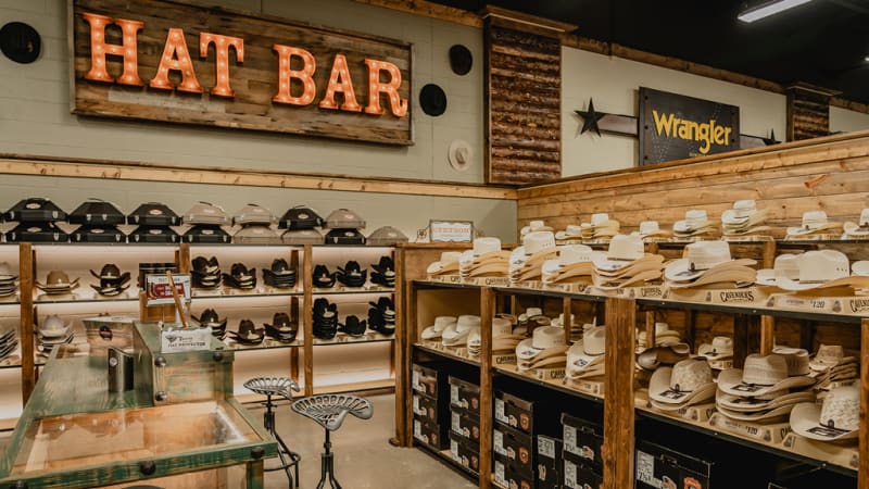 A variety of cowboy hats available at Cavender's Hat Bar, displayed on shelves with hat boxes beneath.