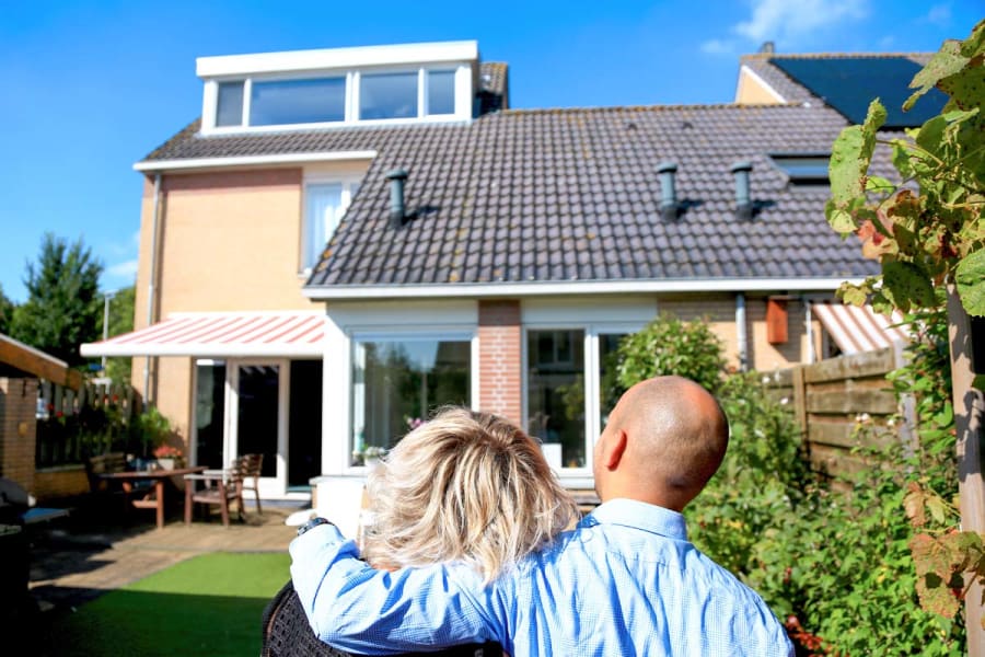 Afbeelding van twee mensen die gearmd naar een huis kijken op een zonnige dag. De afbeelding ondersteunt een kader dat linkt naar een topic over subsidies en leningen voor energiebesparende maatregelen op de homepage van het dossier energie vergelijken.