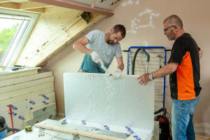 Afbeelding van twee mannen die een isolatieplaat op maat snijden. De afbeelding ondersteunt een kader dat linkt naar een topic over isoleren van woningen op de homepage van het dossier energie vergelijken.