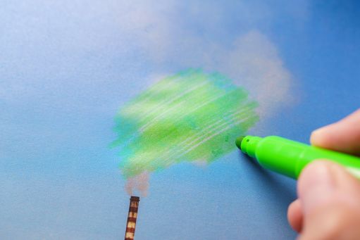 A hand holding a green marker, coloring in gray smoke that's pouring out of a smokestack
