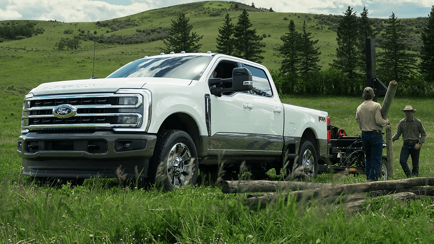 Two people loading logs into a parked Ford F-350
