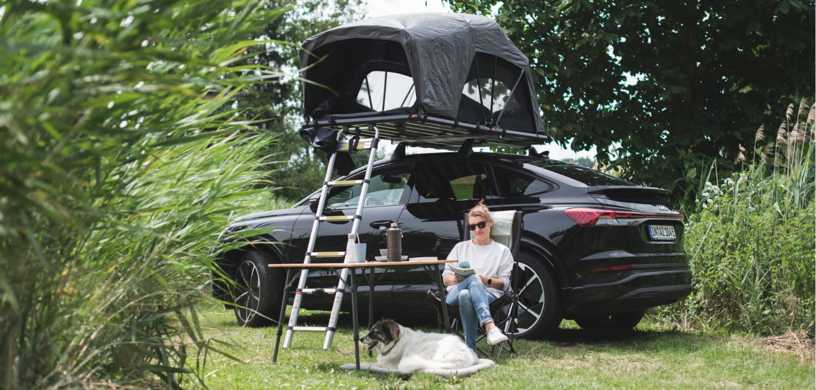 Frau beim Camping im Grünen mit Dachzelt und Hund
