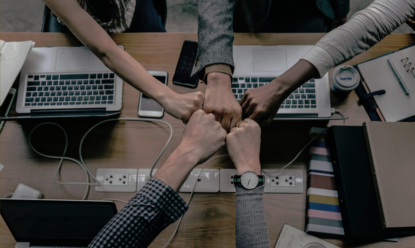 a team shares a fist-bump over a table containing multiple laptops