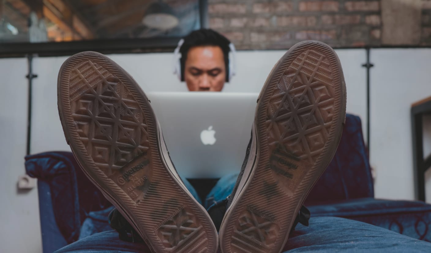 a developer wearing Converse shoes works while sitting on a blue couch