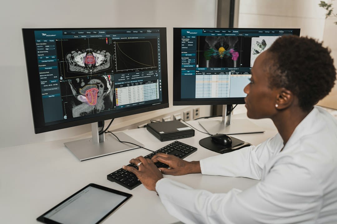 A person in a white coat typing on a keyboard at two medical monitors