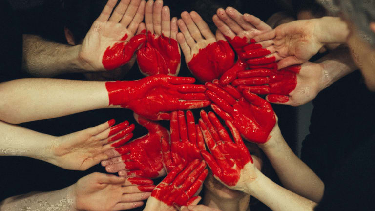 Multiple hands painted red forming a heart shape, symbolizing unity and collective action for good causes.