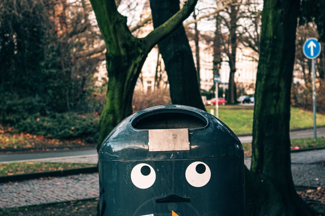 green outdoor garbage bin with face near tree during daytime