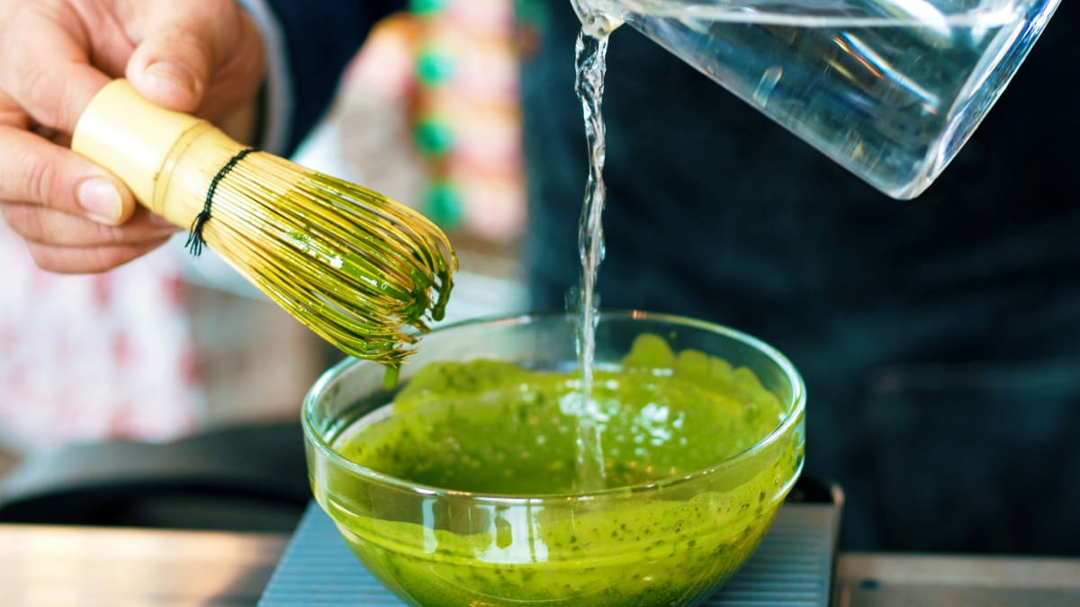 Pouring hot water from a kettle into a matcha bowl