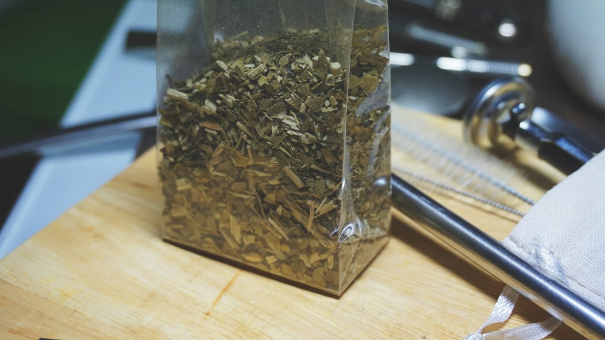 Clear bag of loose yerba mate on a wooden board with a bombilla