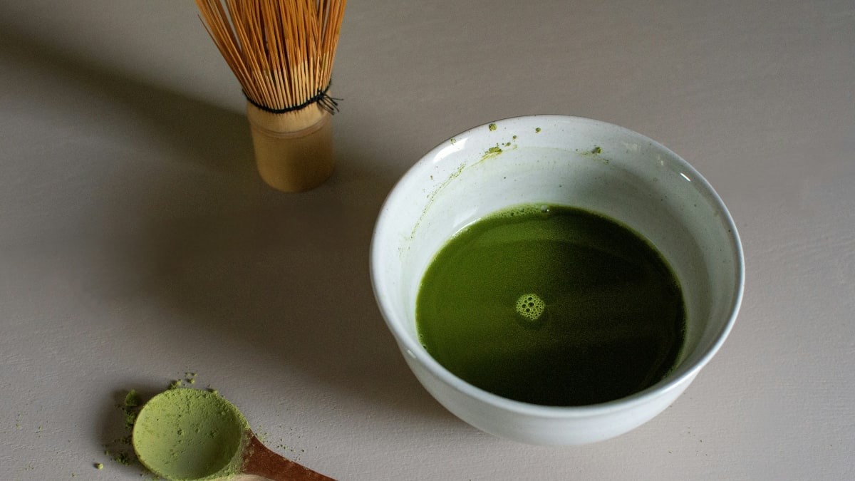 Matcha starter kit: frothy matcha in a ceramic bowl next to a bamboo whisk