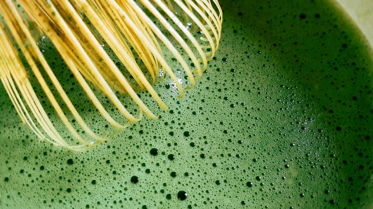 A bamboo chasen whisking frothy matcha in a bowl