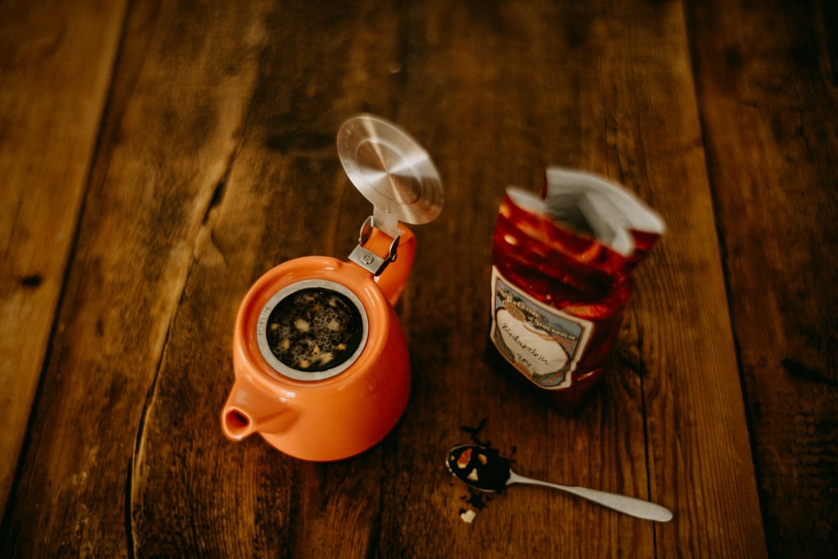 Orange teapot with tea and a spoon on a table