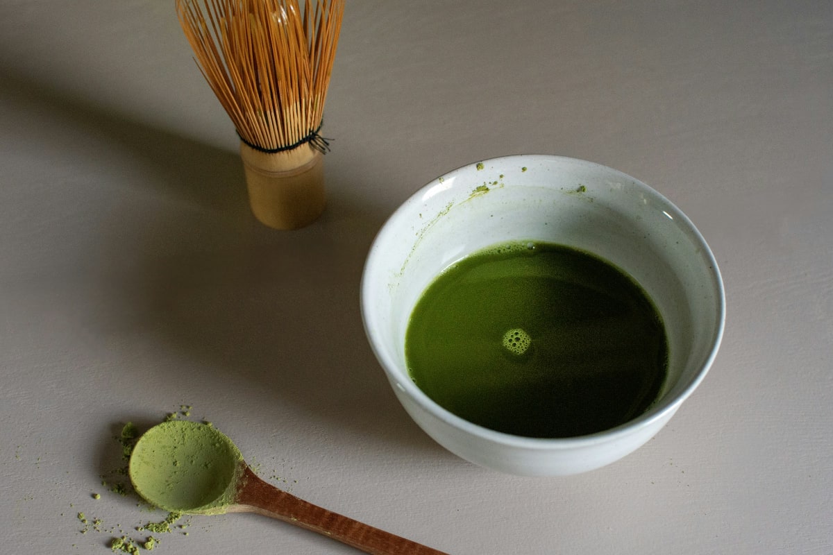 A bowl of matcha next to a bamboo whisk, a chasen
