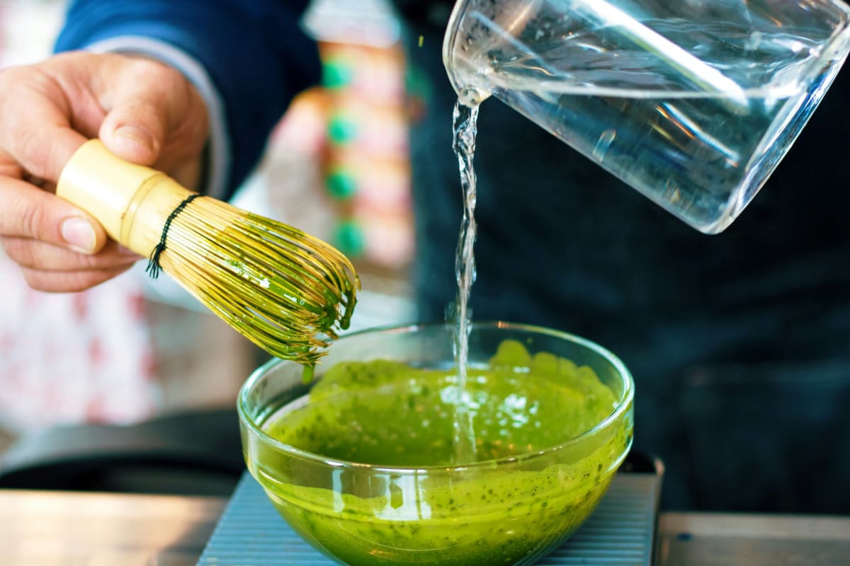 Pouring hot water from a kettle into a matcha bowl