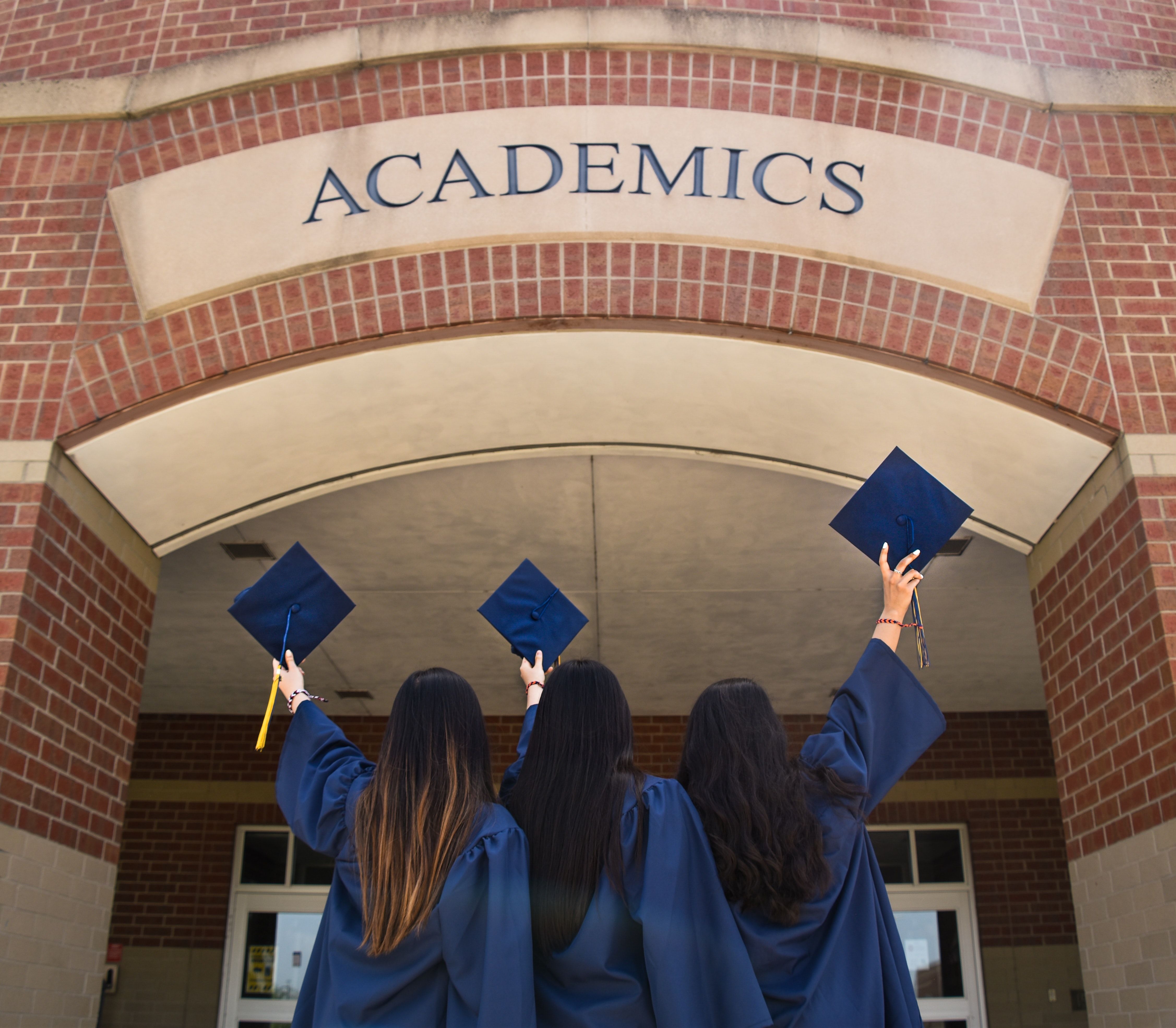 Three women are standing backwards and holding mortarboard hats during graduation. Three women are standing backwards and holding mortarboard hats during graduation.