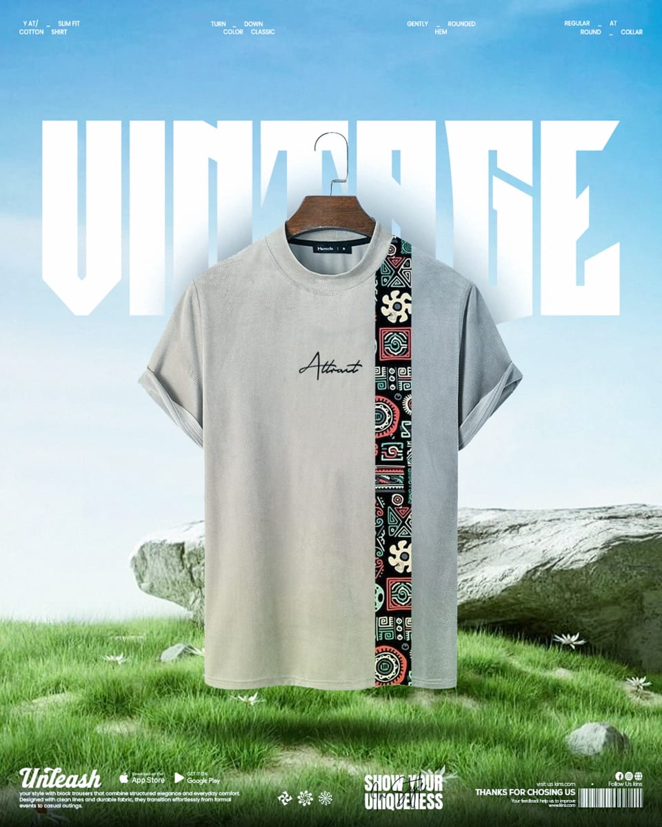 A light grey t-shirt featuring a vertical strip of colorful tribal patterns, floating above a serene grassy field with a large rock, backed by the bold white word "VINTAGE."