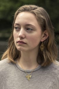 Woman wearing small gold triangle-shaped pendant and diamond-shaped gold drop earrings