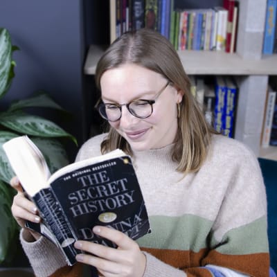 Charlotte smiling while reading a well-thumbed copy of The Secret History by Donna Tartt.