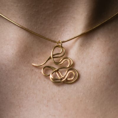 Close-up of a small gold pendant on a neck. The pendant is made out of swirly wire-forms.