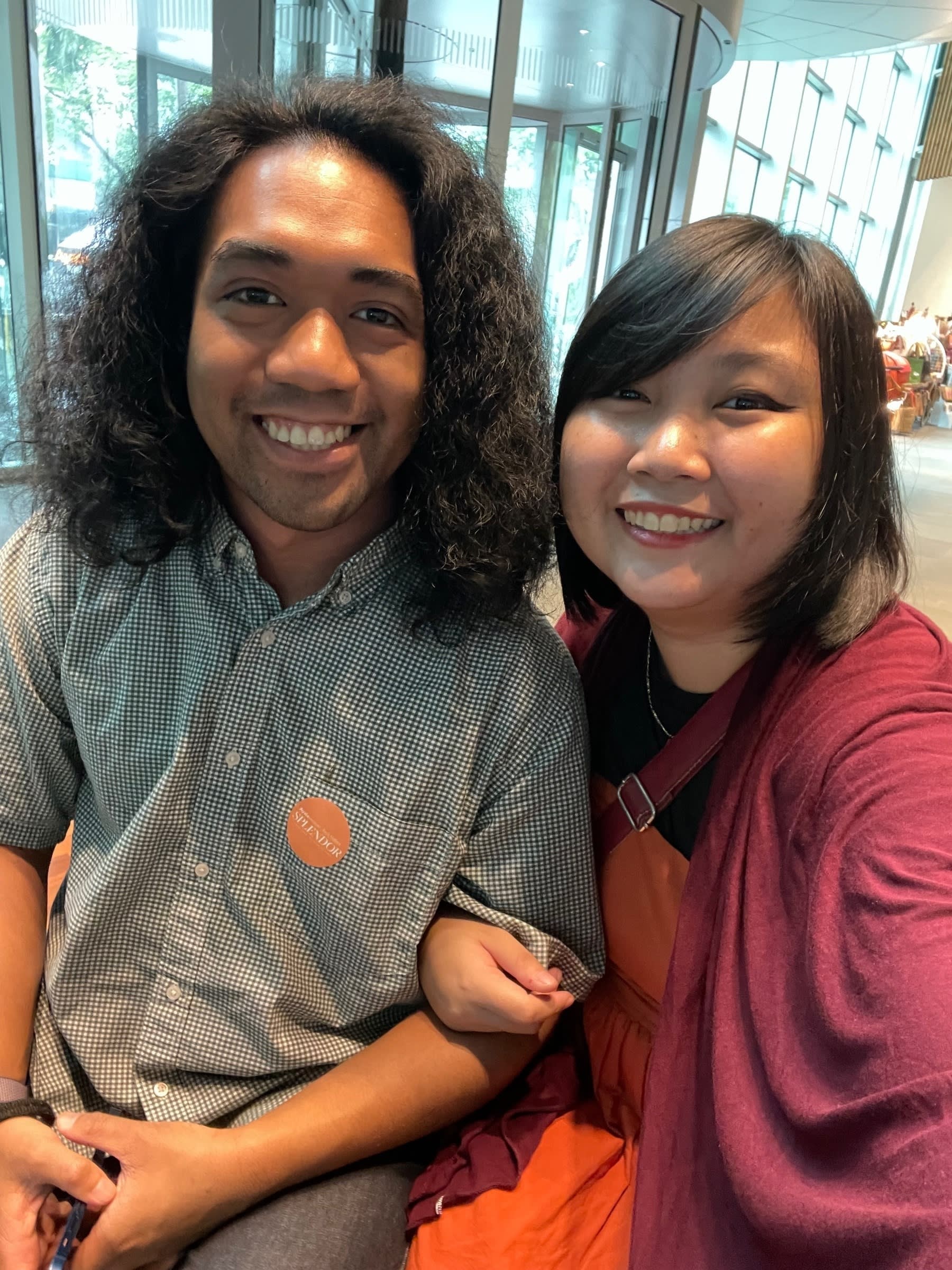 Selfie of Chi and Richard, her boyfriend, together at the lobby of Ayala Museum for a date. Richard has a “SPLENDOR” orange sticker on his right chest pocket, which is the museum's way of identifying visitors for the Splendor exhibit. Chi's hand is wrapped around Richard's, with her other hand off camera, holding the phone to take the photo.