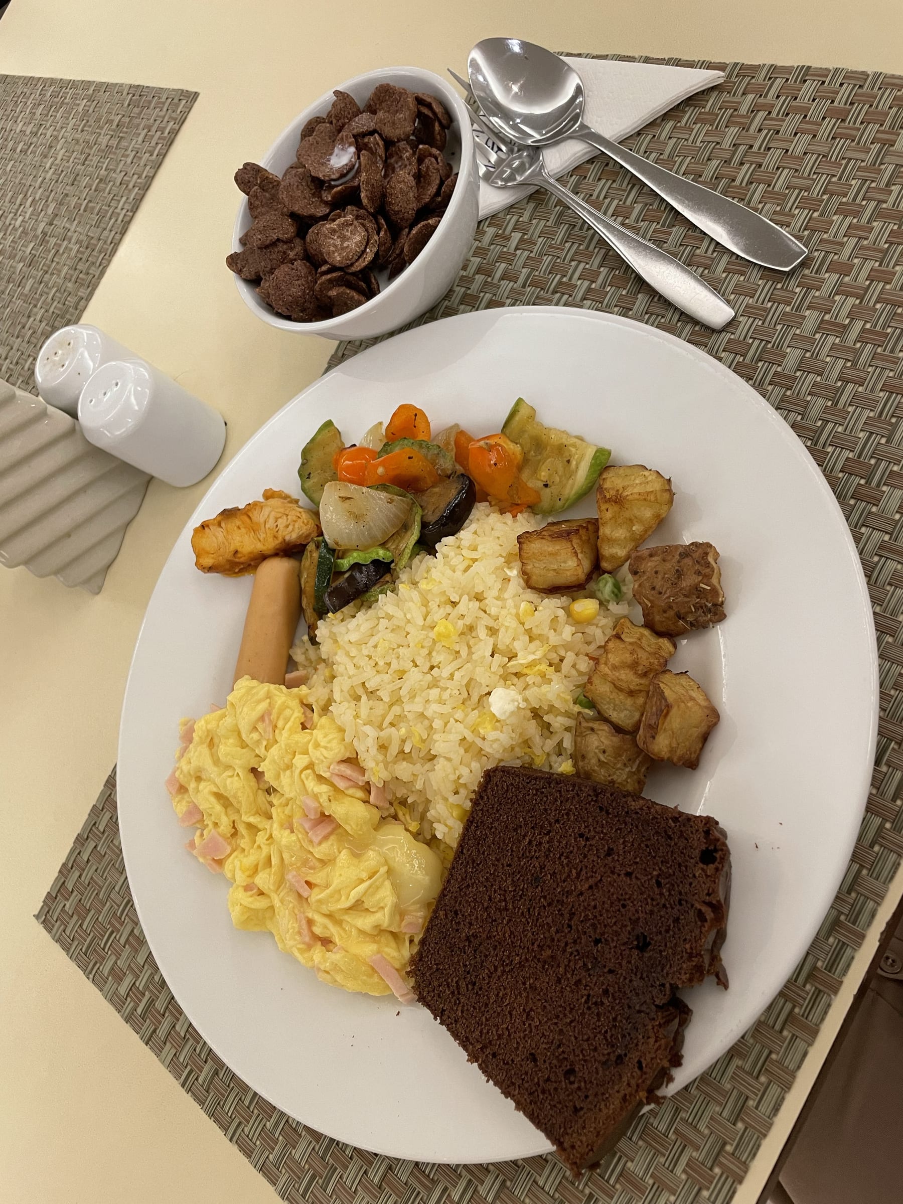 Chi's breakfast from the hotel: scrambled egg with ham and cheese, a chicken sausage, some steamed vegetables, sweet and sour fish, with egg fried rice and a brownie. She also has a bowl of Koko Crunch chocolate cereal.