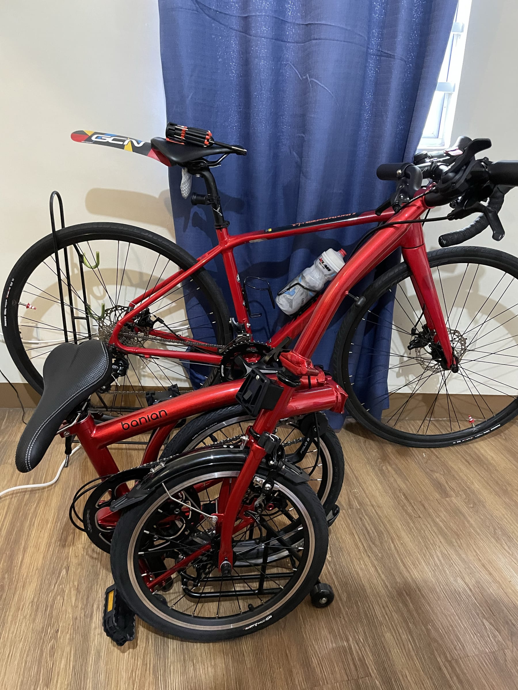 photo of Chi's two bikes, a red Merida Scultura 200 Disc road bike at the back, and a folded Banian Trifold 16" bike