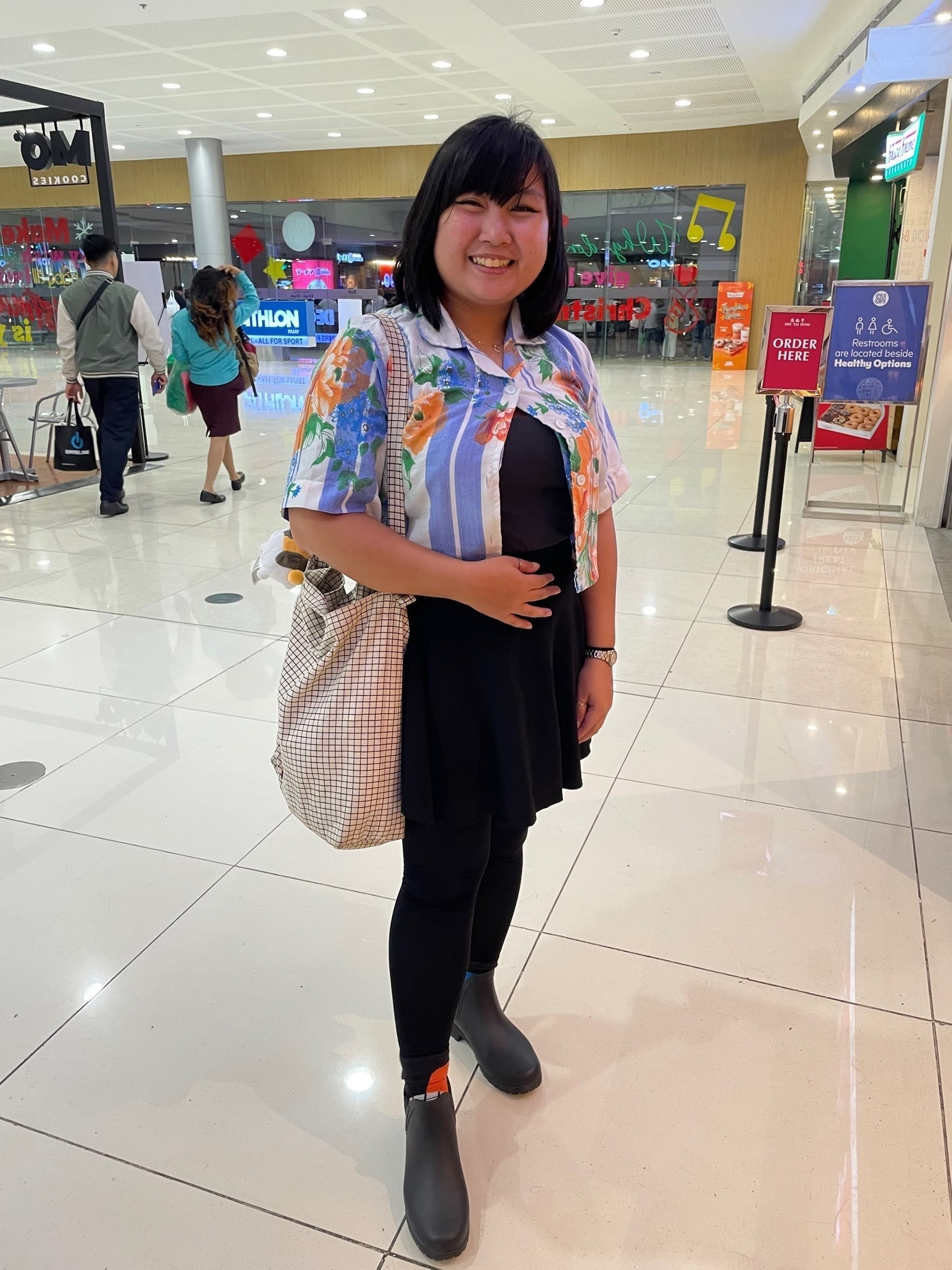 Chi’s full outfit. Her top is a cropped button top of what looks similar to blankets that were popularly used for bed when she was a child, with a black undergarment and a black skater skirt. She’s also wearing black stockings and black boots, with her Figma two-toned orange and blue socks peeking above her boots. On her shoulder is her Figma grid tote bag.