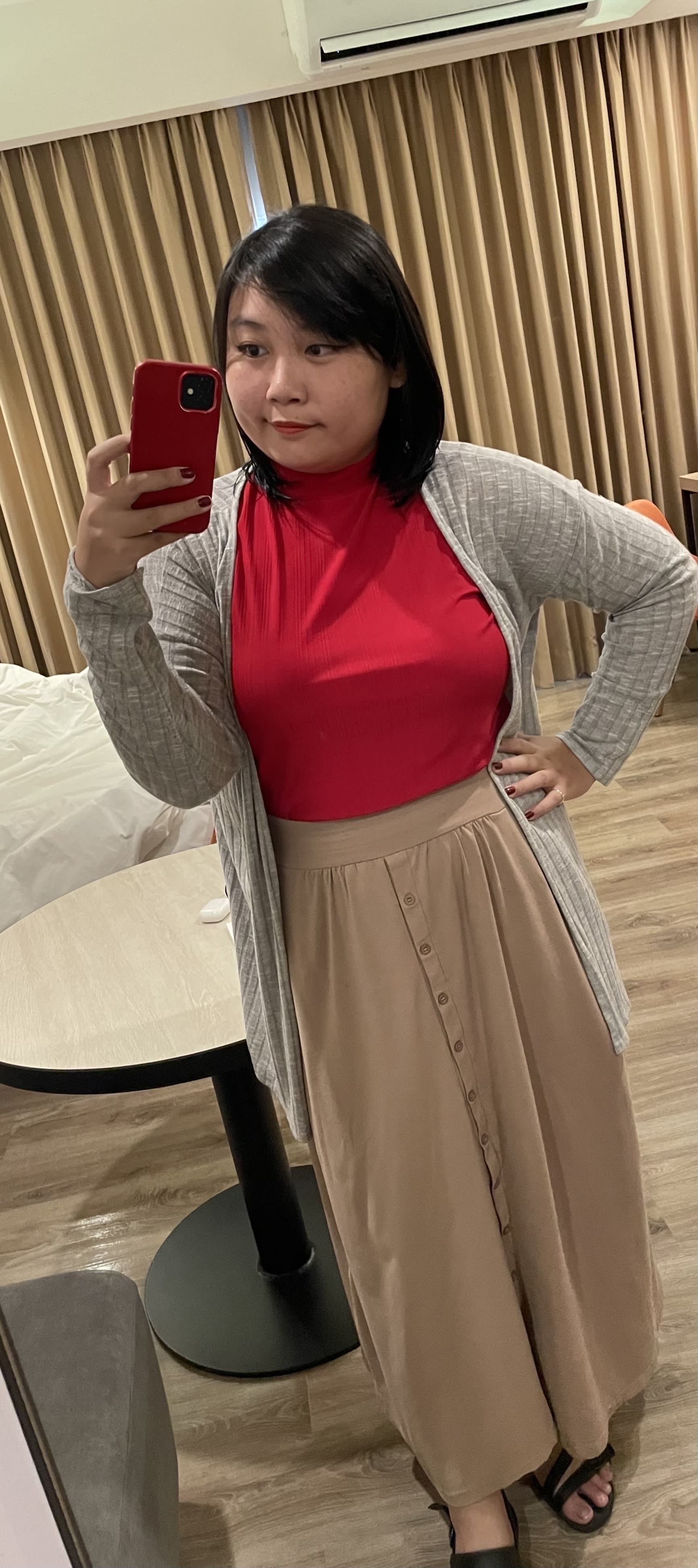 Chi’s ouftit, which is a red turtleneck sheer top tucked in her long beige skirt, and with a gray cardigan and black sandals. She’s also wearing her signature makeup look, which is cat eye eyeliner and red lipstick.