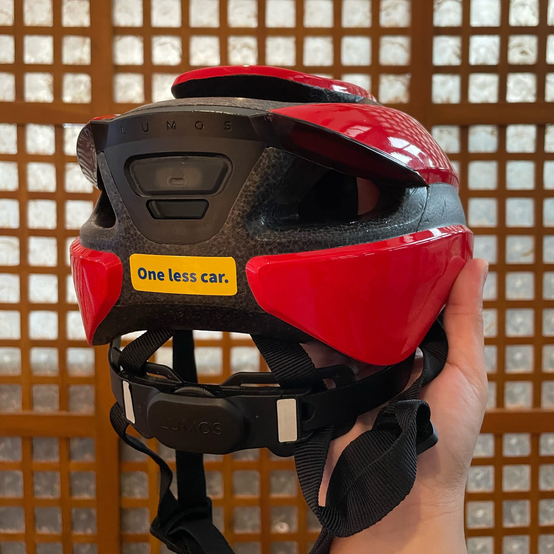 photo of the back of a red Lumos helmet, with the sticker "One less car" shown