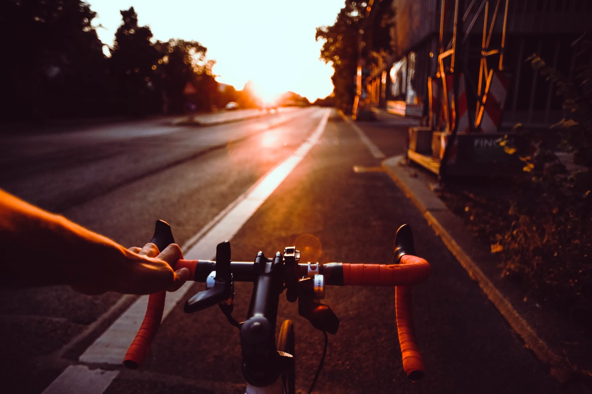 point-of-view of someone on a road bike, where the handlebars are visible, peering out to the road in front of them. A bit of sunlight is reflecting on the asphalt of the road, which somewhat encourages you to press on.