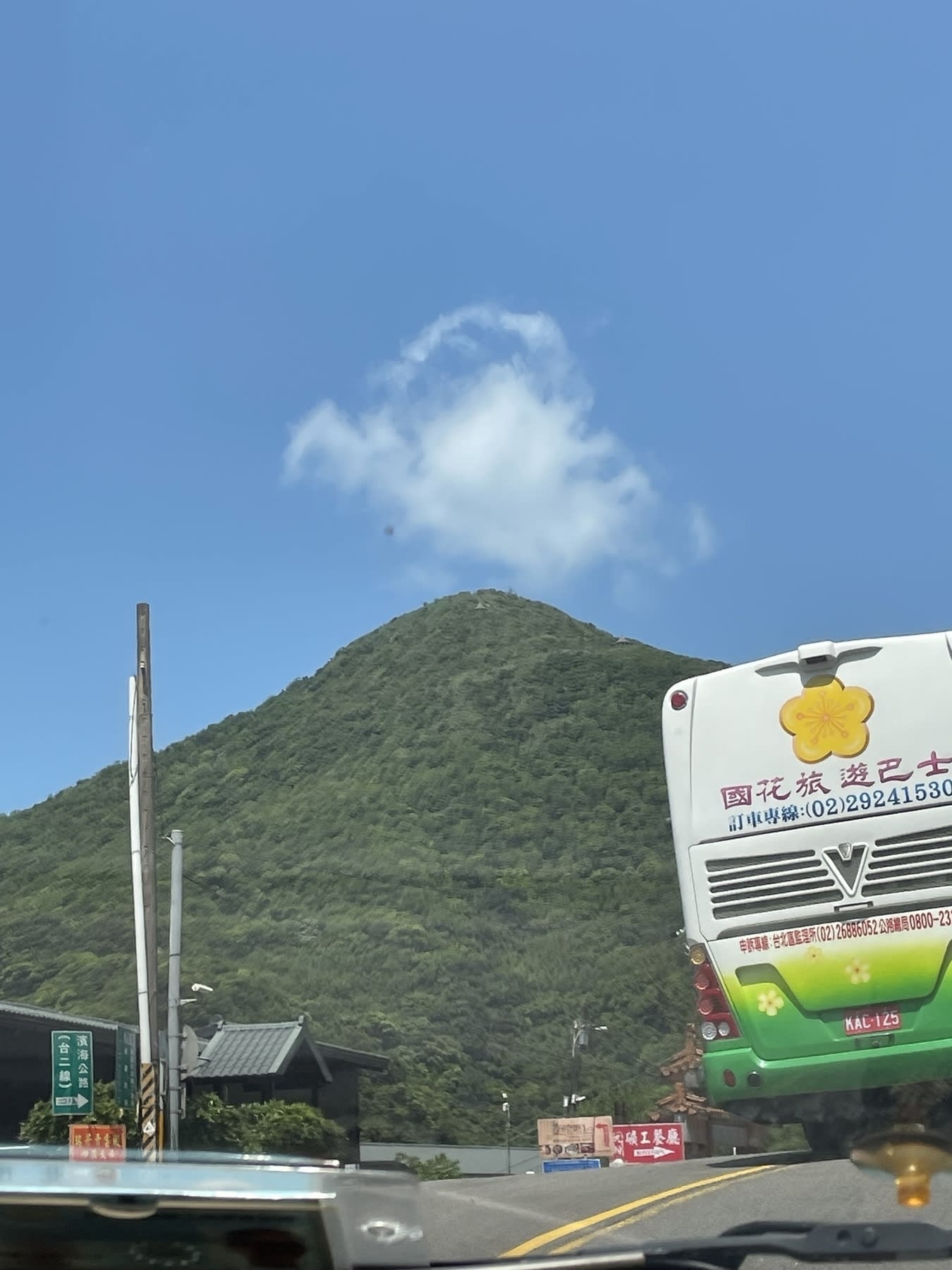 A mountain covered with vegetation near Jioufen in Taiwan. A small thin cloud is seen on the tip of the mountain. A bus is seen on the right side of the photo because Chi took this as she was seated on the front passenger seat while going up the road.
