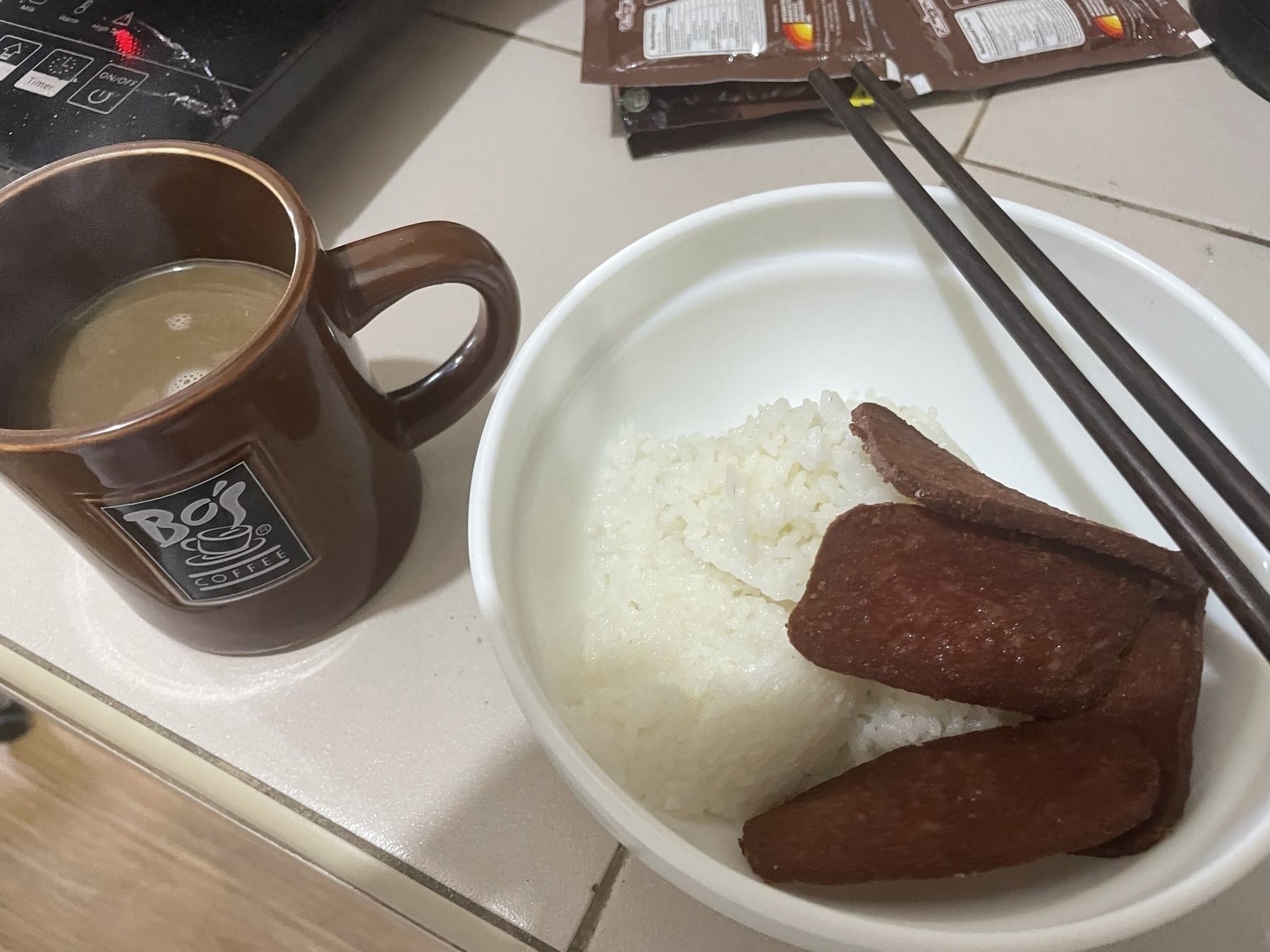Chi’s usual breakfast meal, which is a hot coffee with sugar and creamer and fried luncheon meat with a couple of scoops of rice. Her utensils are chopsticks, and her meal is placed in a bowl.