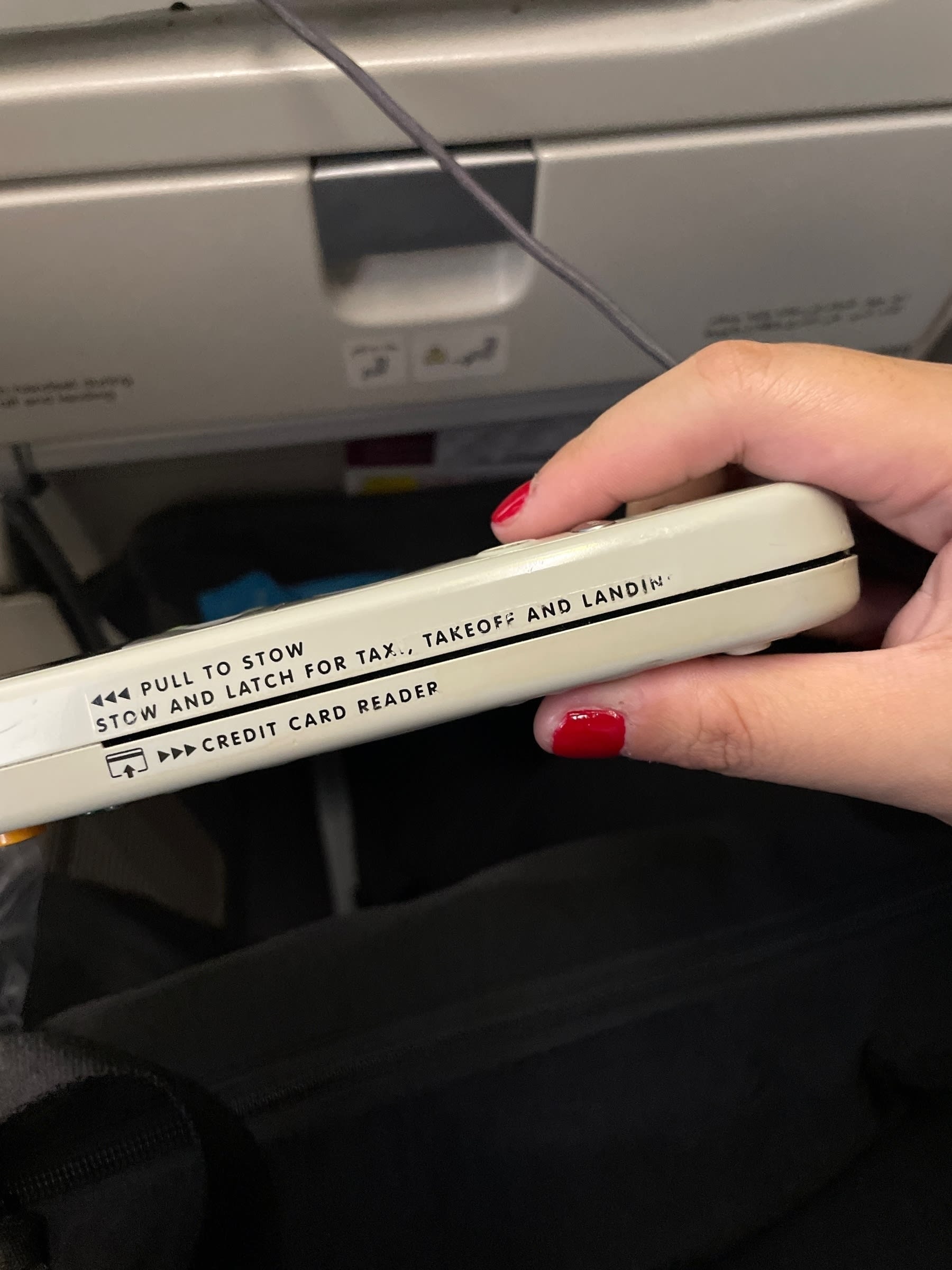 A credit card reader seen on the side of the remote available for in-flight entertainment in an airplane. The text above the card slot reads: “Pull to Stow | Stow and Latch for taxi, takeoff and landing”
