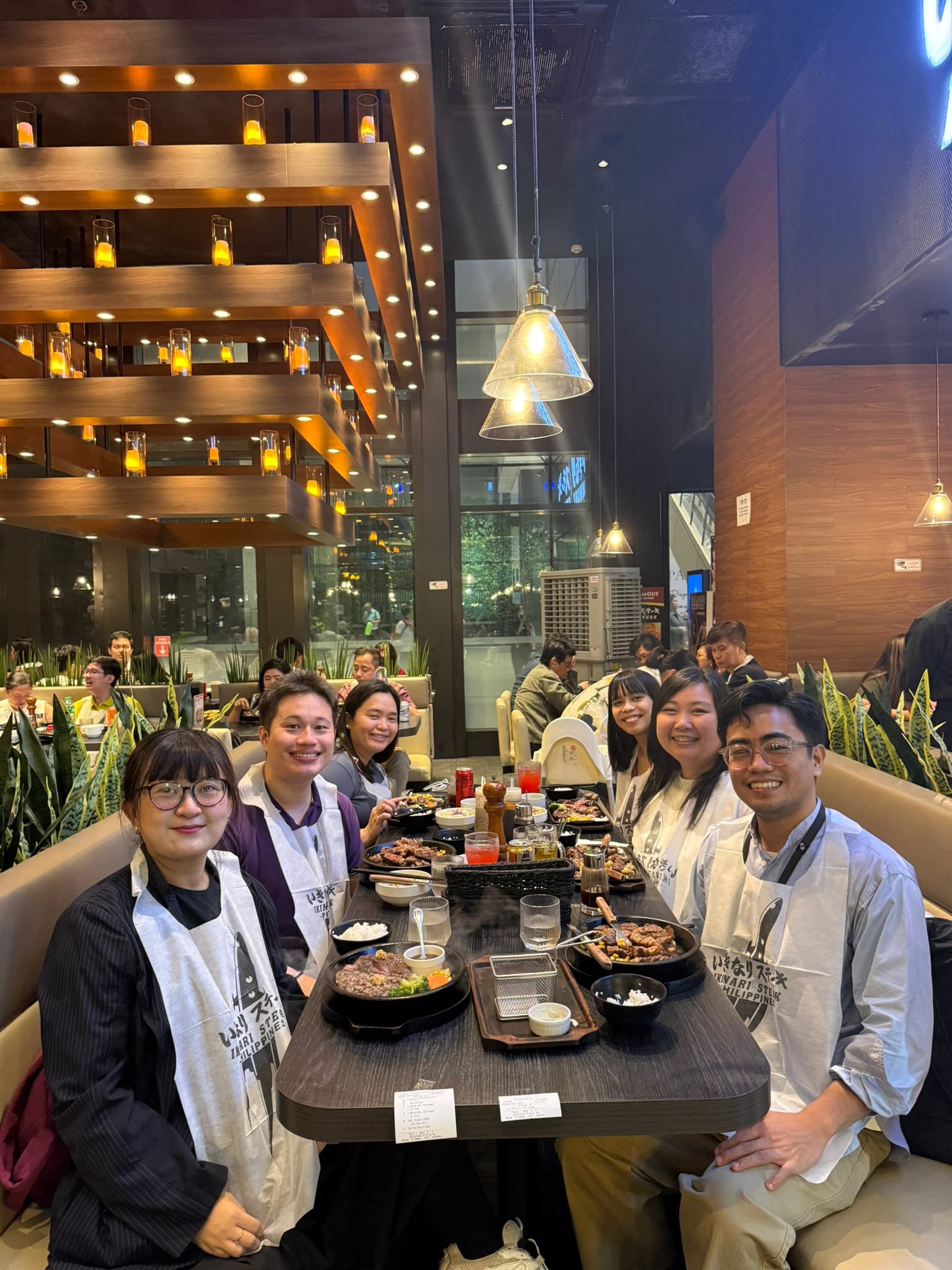 Group photo of volunteers from FoF Manila with each person having a bib from Ikinari Steak over their chest and their food orders are placed in front of them on the table.