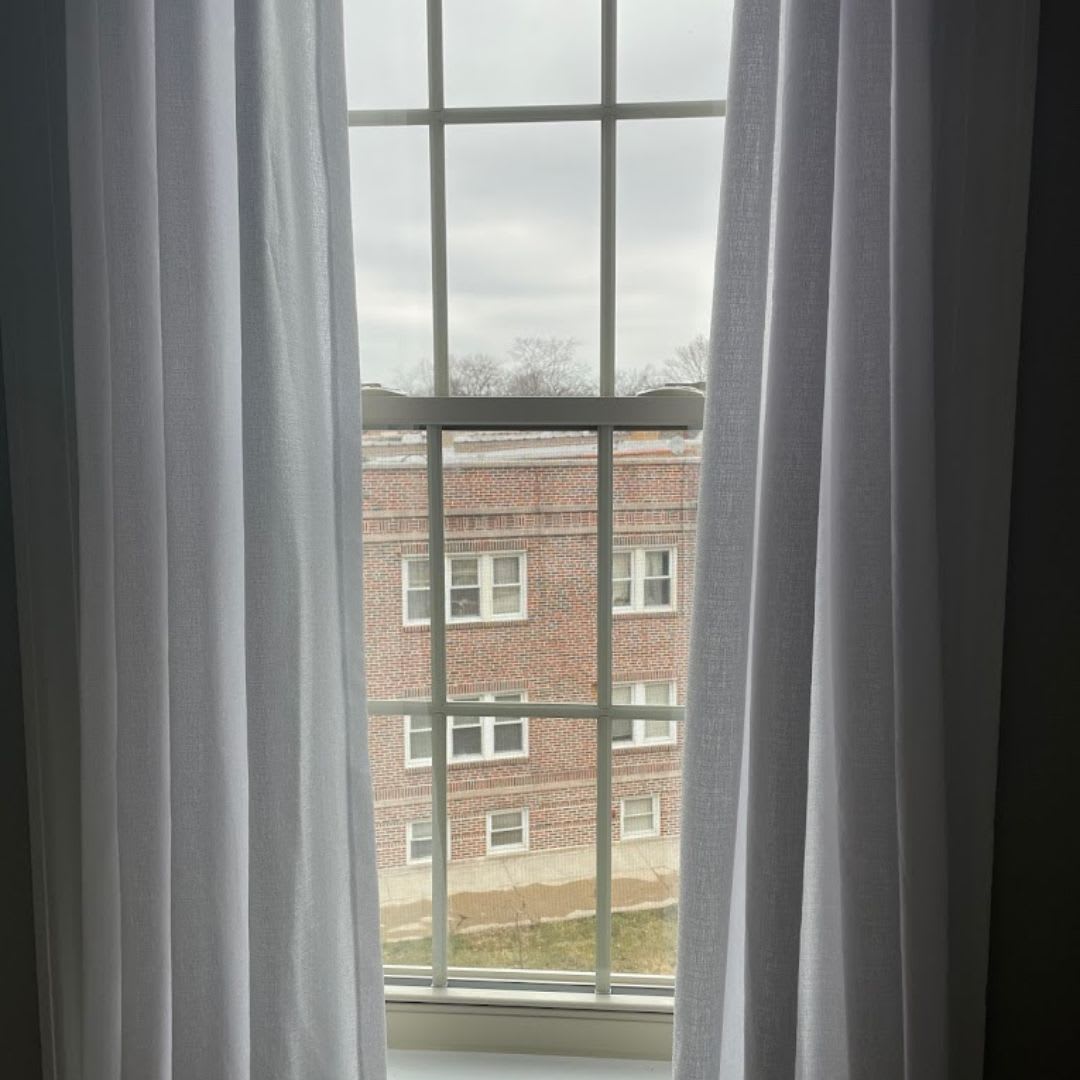 A window with white curtains and a view of a building.
