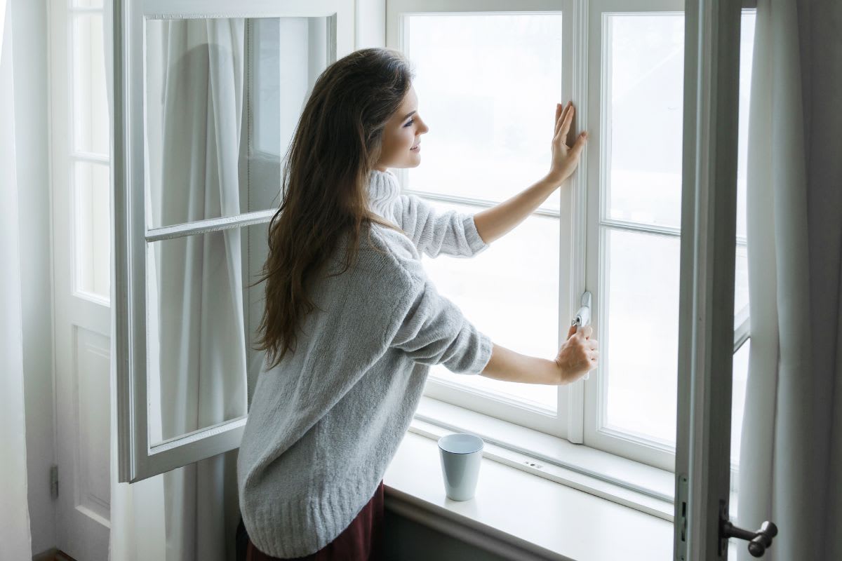 A woman looking out a window with a cup of coffee.