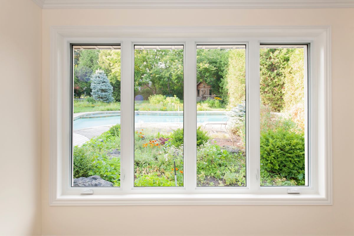 View of a garden and pool through a four-paneled window from inside a room.