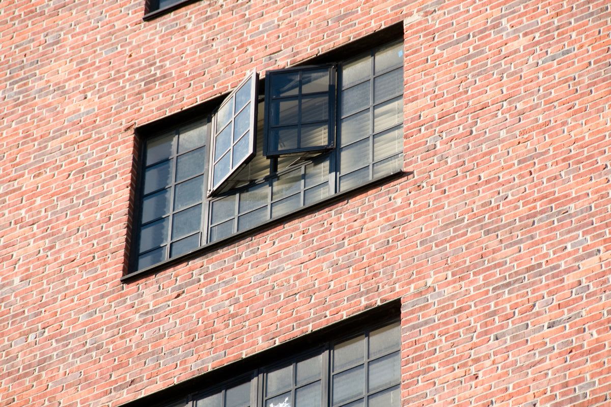 A brick building with two visible windows, one partially open, reflecting sunlight.