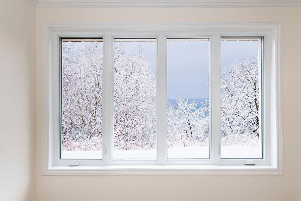 A view of a snow-covered landscape through a four-paneled window, with icy trees and a glimpse of the ocean in the background.