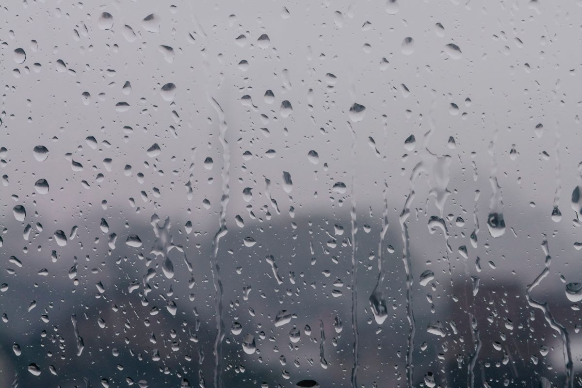 Raindrops cover a window with a blurred view of a gray, overcast landscape in the background.