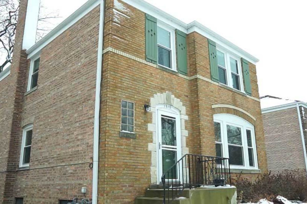 Two-story brick house with green shutters, arched front door, black railing, fresh window replacement in Evanston, and snow on the ground.
