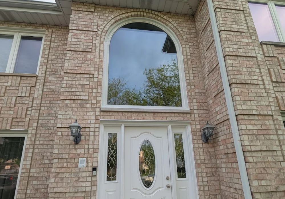 A large arched window is positioned above a white front door with decorative glass panels on a brick house exterior. Two wall-mounted lanterns flank the door.