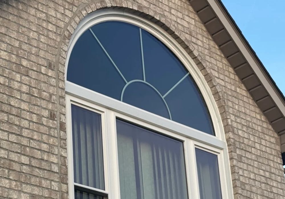 Arched window with a decorative sunburst design above a rectangular window on a brick building exterior.