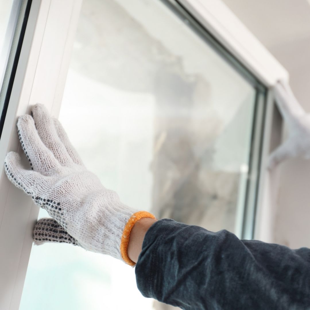 A person wearing white work gloves is installing or adjusting a bow window frame during a bow window installation.