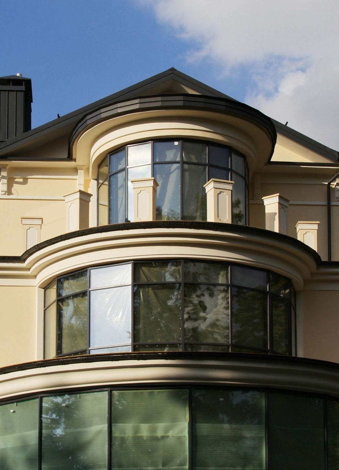 Modern beige building facade with large bow windows, decorative columns, and a triangular roof against a blue sky with some clouds—an impressive design that reflects expert craftsmanship like that of Chicago Window Guys.