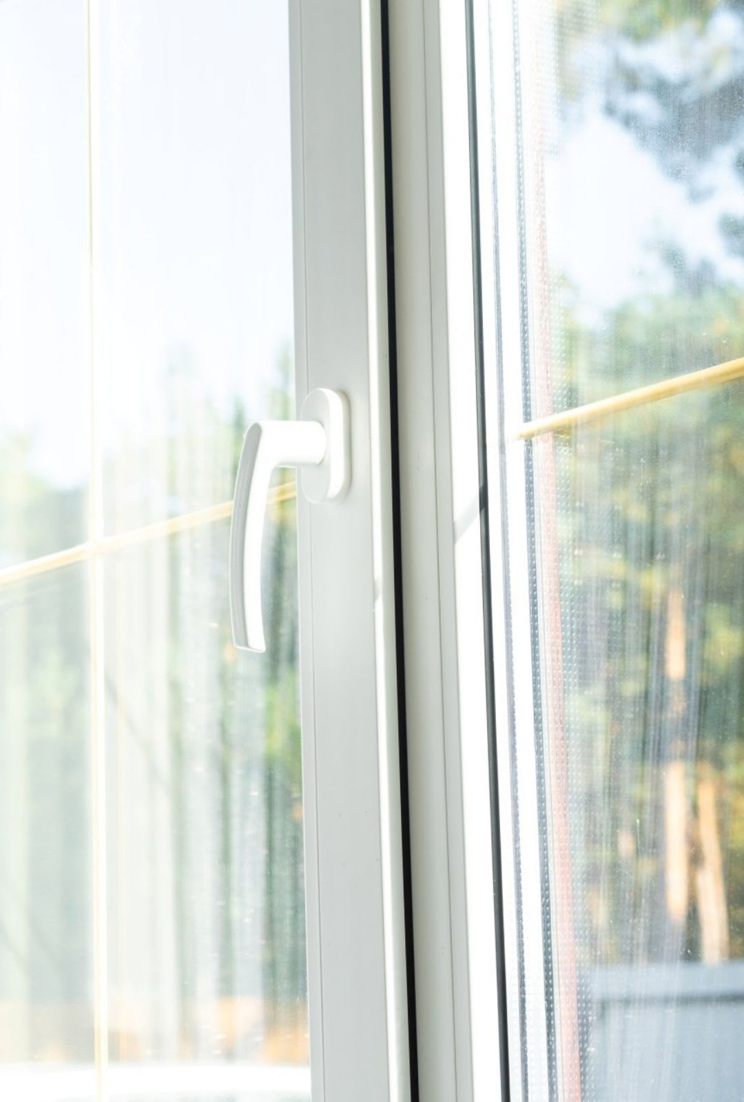 A close-up of a white handle on a glass sliding door, with an outdoor scene and greenery faintly visible—showcasing the sleek style you can expect from Chicago Window Guys' expert window installation.