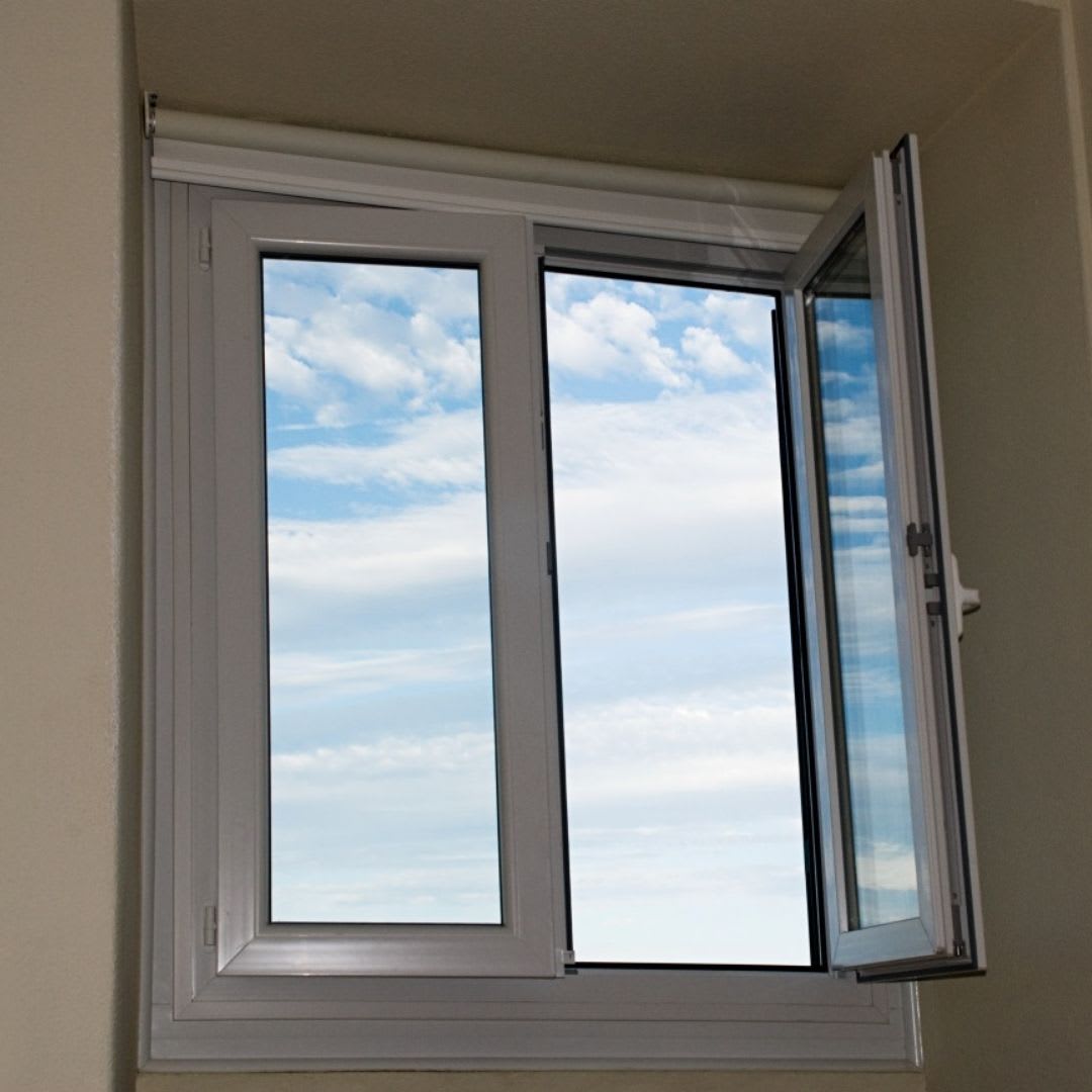 A white-framed casement window set in a beige wall, with one panel open, shows a blue sky with scattered clouds—an inviting example of the craftsmanship offered by Chicago Window Guys.