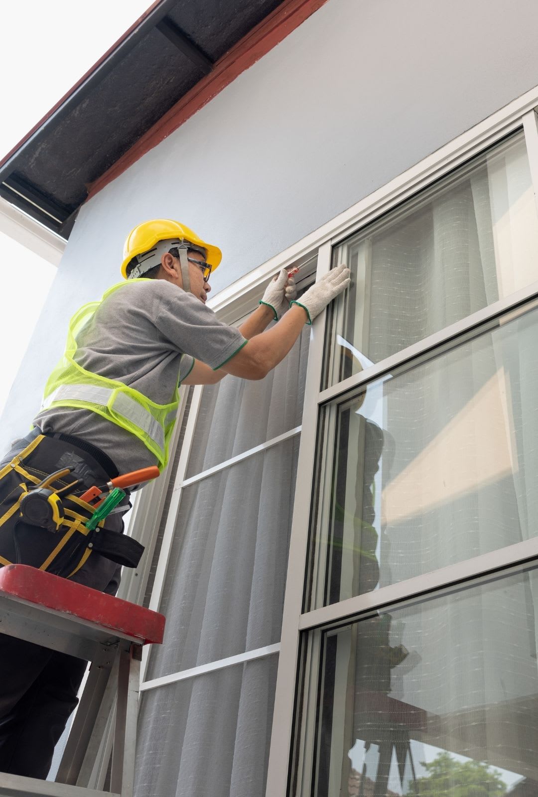 A construction worker wearing safety gear installs or repairs a window from a stepladder outside a building, showcasing the expertise of Chicago Window Guys.