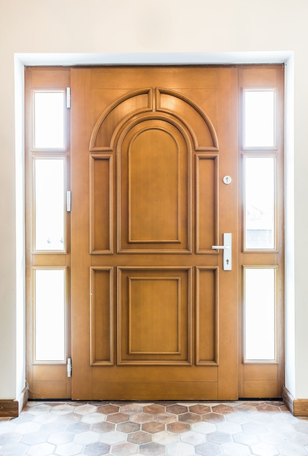 A closed wooden front door with decorative panels and arched design, flanked by narrow glass windows on both sides, set in a light-colored wall—perfect inspiration for fiberglass entry doors or modern entry doors Chicago homeowners love. Fiberglass entry doors in Chicago
