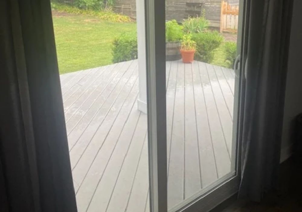 A sliding glass door is partially open, leading to a gray wooden deck and a grassy backyard with plants and a potted flower.